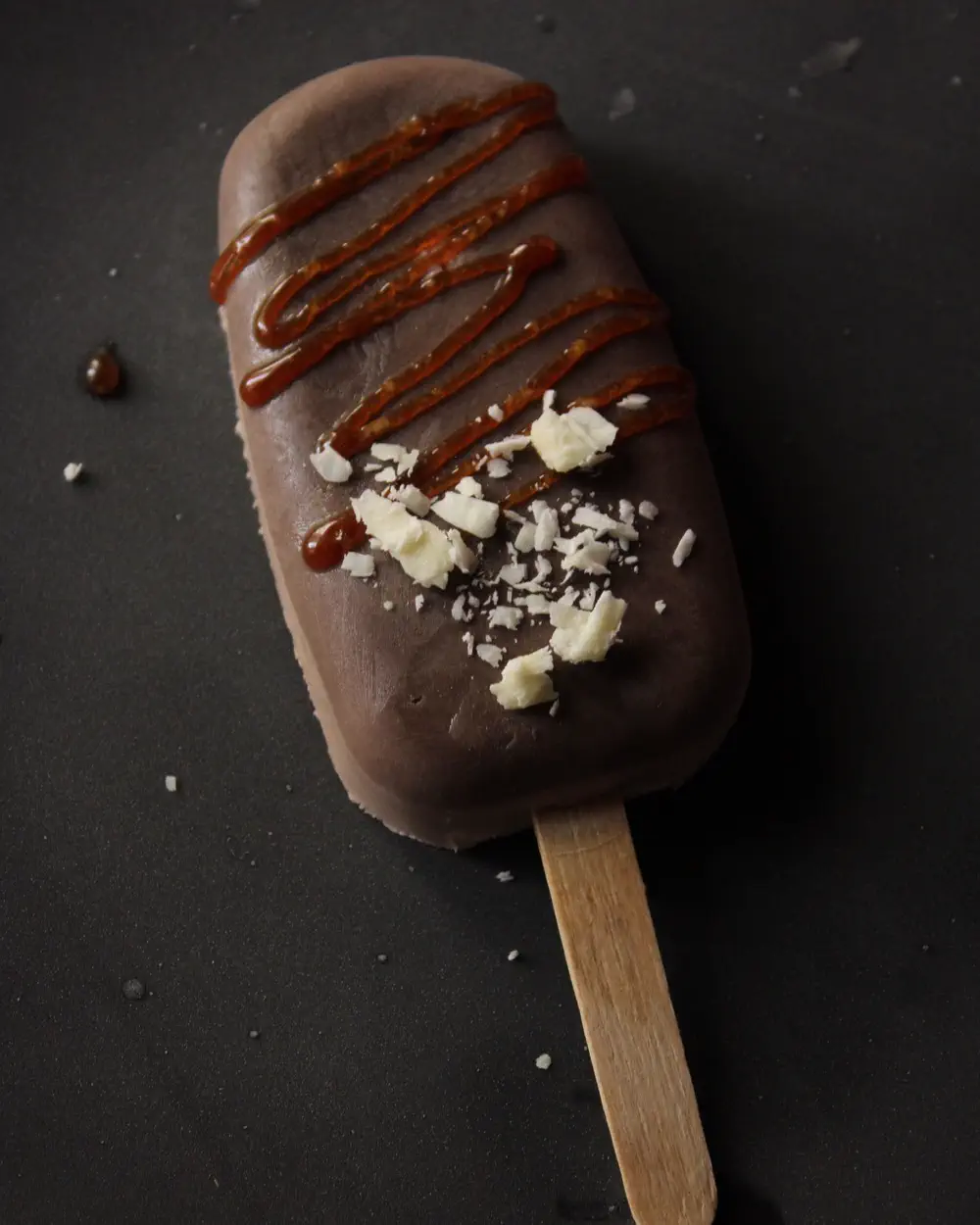 A chocolate-coated ice cream bar with caramel drizzle on a dark surface