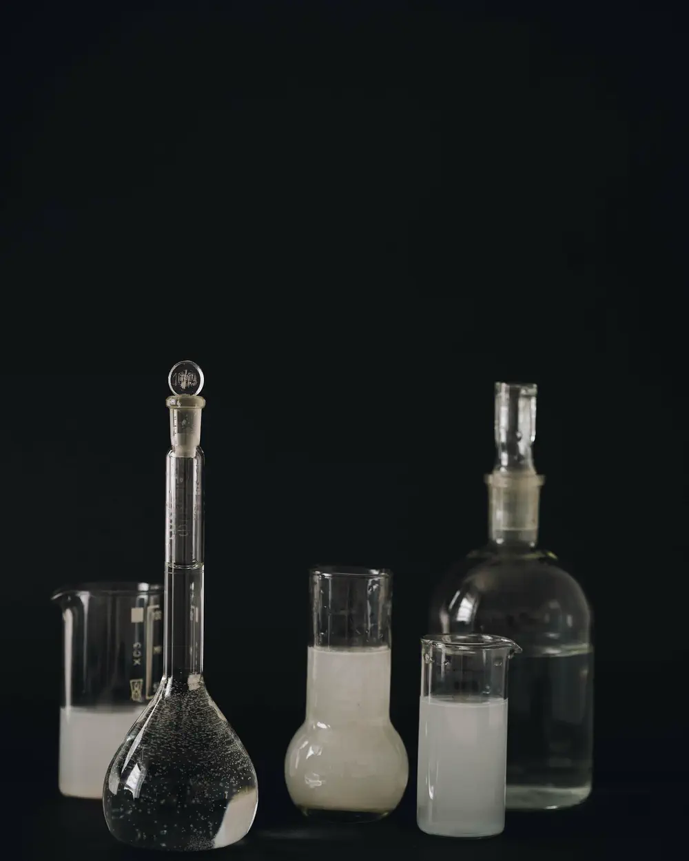 Laboratory glassware holding cloudy and clear liquids on a black surface