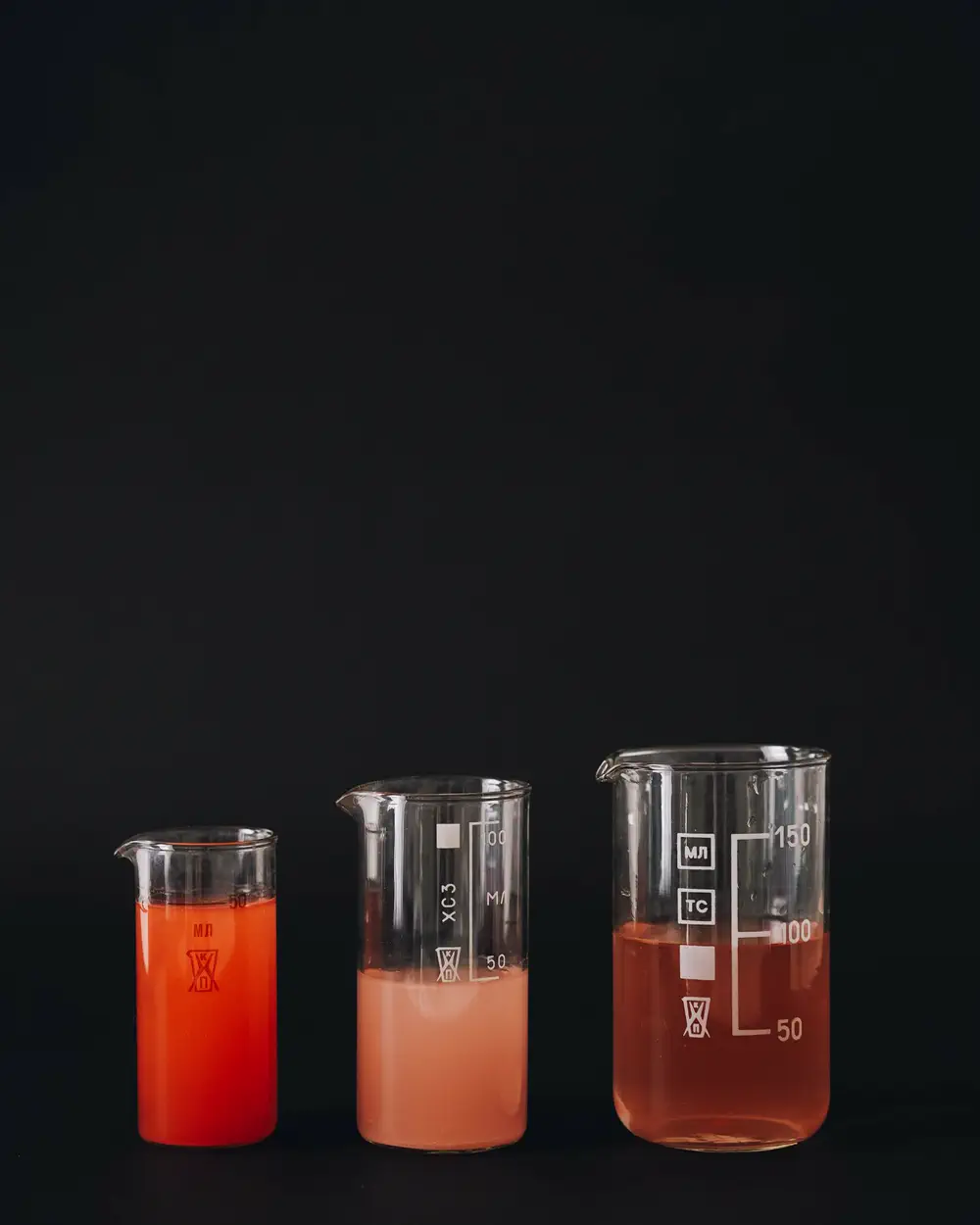 Three graduated beakers holding red liquid at different levels