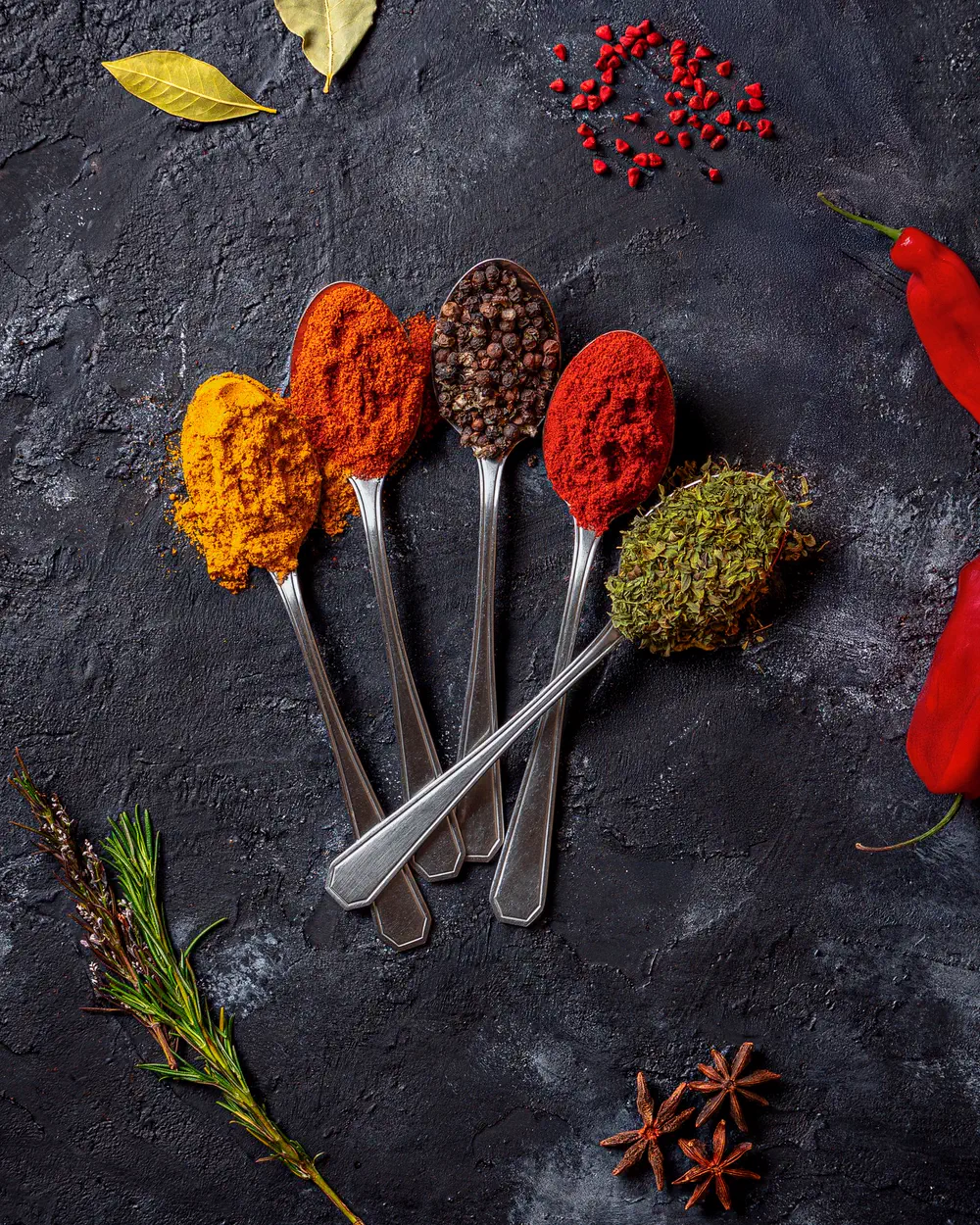 Spoons of ground spices on a dark slate surface