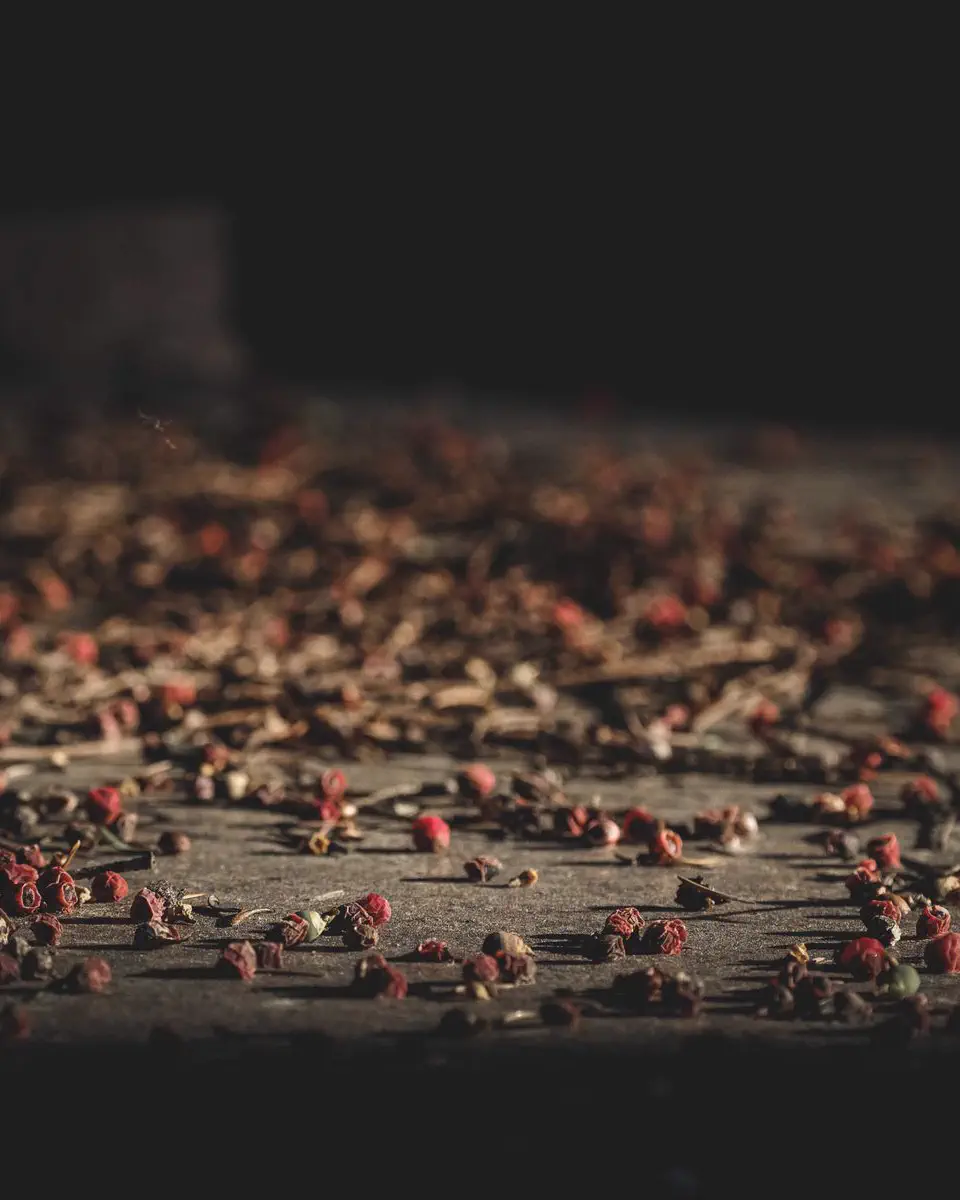 Pink peppercorns scattered across a dark wooden surface
